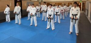 Taekwon-Do candidates standing in rows on blue mats at the UTA black belt grading in Hitchin.